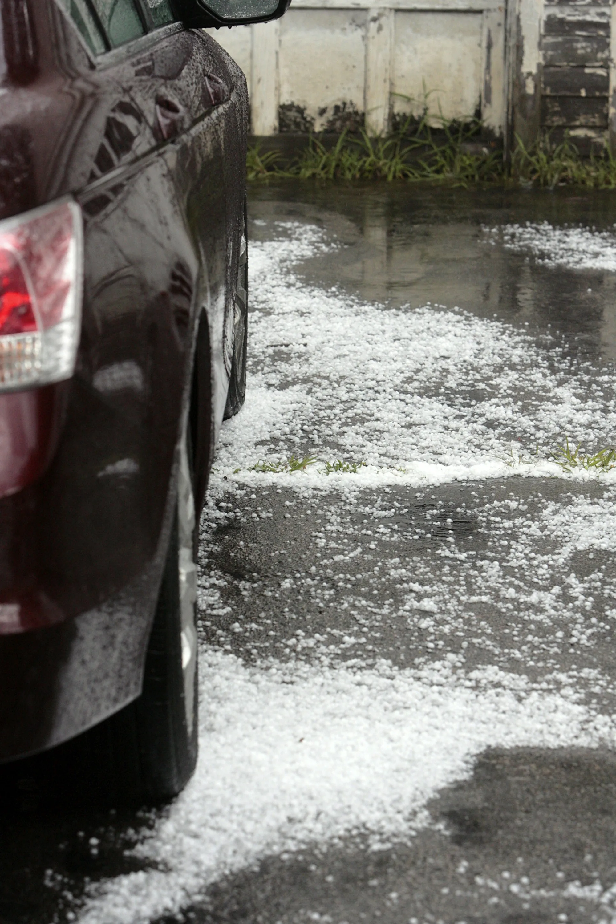 Hailstones scattered on wet pavement beside a parked car